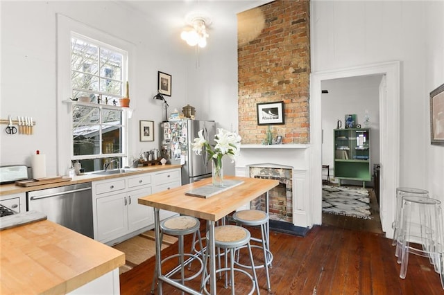 kitchen with butcher block counters, white cabinetry, a breakfast bar area, a fireplace, and appliances with stainless steel finishes