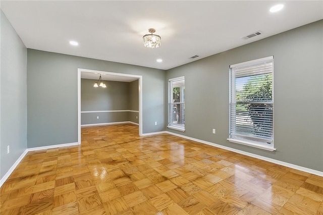 empty room featuring light parquet flooring, a healthy amount of sunlight, and an inviting chandelier