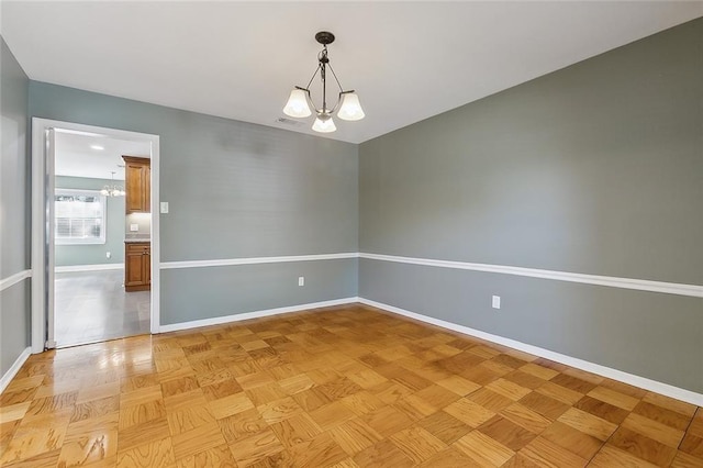 empty room with light parquet floors and a notable chandelier