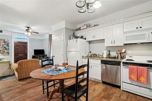 kitchen with light stone countertops, ceiling fan with notable chandelier, white appliances, light hardwood / wood-style floors, and white cabinetry