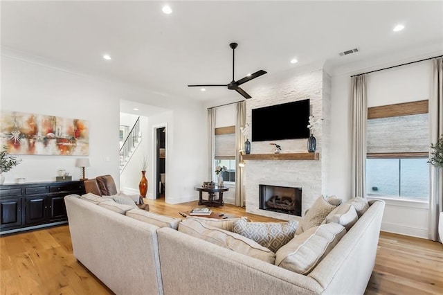 living room with light hardwood / wood-style floors, a stone fireplace, and ceiling fan