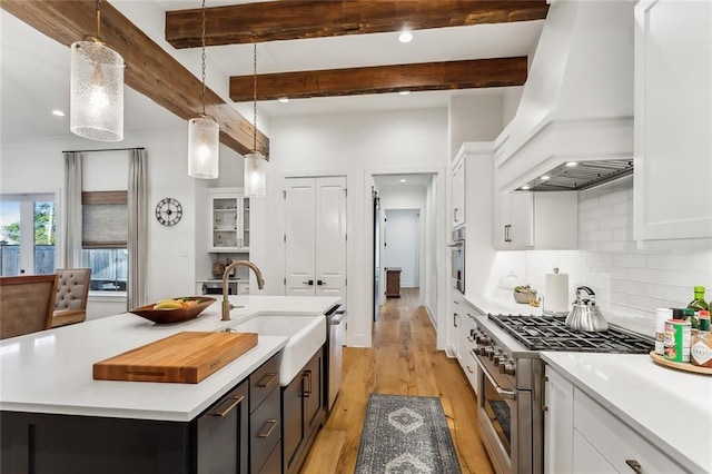 kitchen with appliances with stainless steel finishes, premium range hood, hanging light fixtures, and a kitchen island with sink