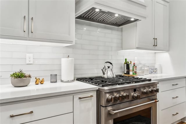 kitchen featuring stainless steel stove, tasteful backsplash, white cabinetry, and custom exhaust hood