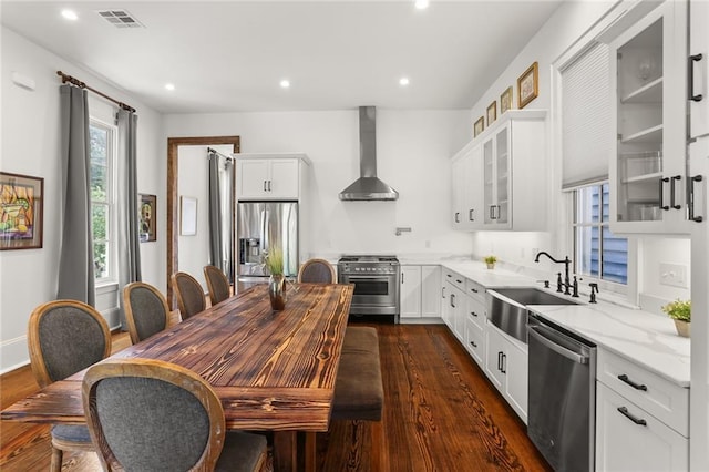 kitchen featuring white cabinets, wall chimney range hood, sink, appliances with stainless steel finishes, and light stone counters