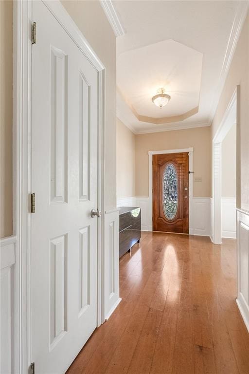 doorway with ornamental molding, a tray ceiling, and light hardwood / wood-style flooring