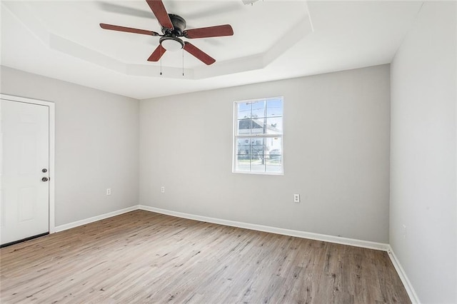 empty room with ceiling fan, light hardwood / wood-style flooring, and a tray ceiling