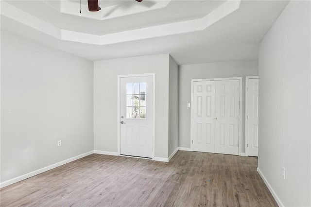 entrance foyer with ceiling fan, wood-type flooring, and a raised ceiling