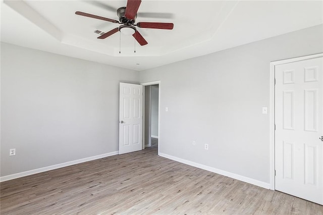 empty room featuring ceiling fan, light hardwood / wood-style flooring, and a tray ceiling