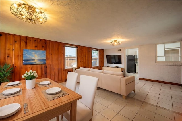 dining space featuring light tile patterned floors, a textured ceiling, and wooden walls