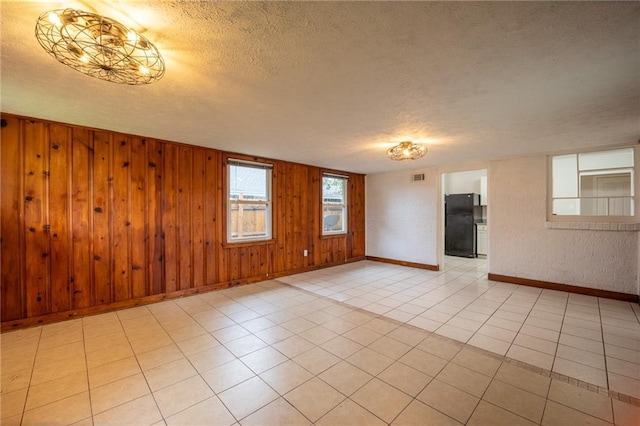 spare room featuring a textured ceiling, wooden walls, and light tile patterned flooring