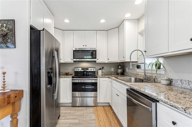 kitchen with light stone countertops, stainless steel appliances, white cabinetry, and sink