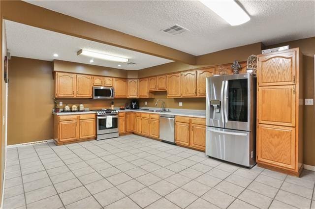 kitchen featuring light tile patterned flooring, a textured ceiling, stainless steel appliances, and sink