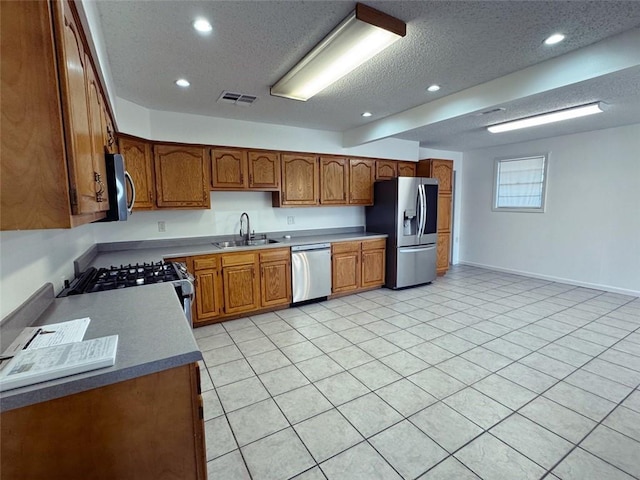 kitchen with visible vents, a sink, brown cabinetry, a textured ceiling, and appliances with stainless steel finishes