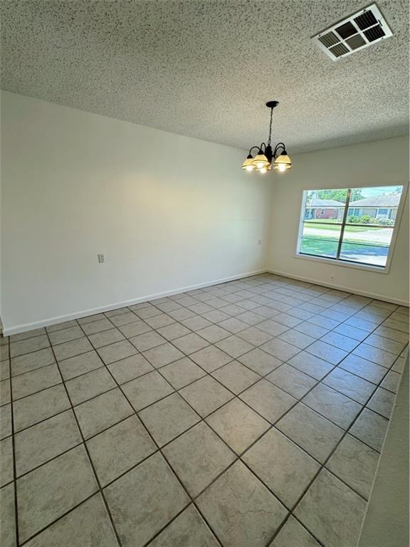 spare room featuring visible vents, light tile patterned flooring, baseboards, a textured ceiling, and a notable chandelier