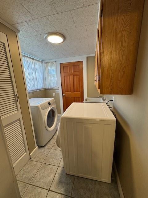 clothes washing area with washer and dryer, baseboards, cabinet space, and light tile patterned floors