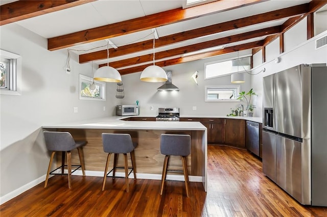 kitchen featuring stainless steel appliances, wall chimney range hood, dark hardwood / wood-style flooring, kitchen peninsula, and pendant lighting