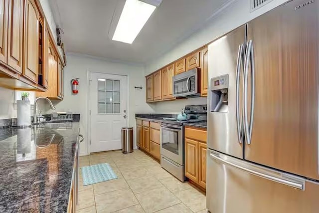 kitchen featuring dark stone countertops, sink, light tile patterned floors, and stainless steel appliances