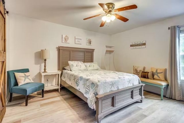 bedroom featuring a barn door, ceiling fan, and hardwood / wood-style flooring