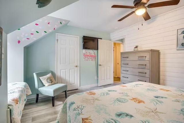 bedroom featuring light hardwood / wood-style floors, ceiling fan, and wooden walls