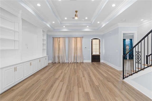 unfurnished living room featuring built in shelves, a tray ceiling, light hardwood / wood-style flooring, and ornamental molding