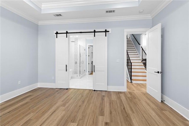 empty room featuring a barn door, crown molding, and light hardwood / wood-style flooring