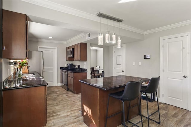 kitchen featuring a kitchen breakfast bar, crown molding, appliances with stainless steel finishes, decorative light fixtures, and a kitchen island