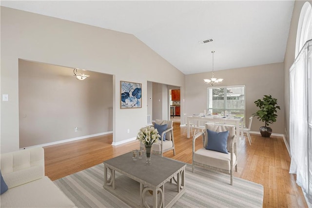 living room with a notable chandelier, light wood-style floors, visible vents, and high vaulted ceiling