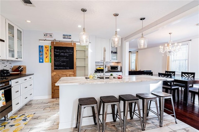 kitchen featuring a kitchen breakfast bar, tasteful backsplash, light stone counters, a kitchen island with sink, and white cabinets