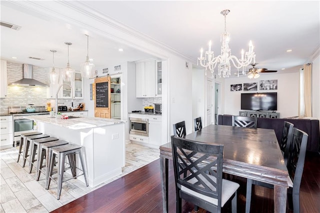 dining area with ceiling fan with notable chandelier, ornamental molding, and light hardwood / wood-style flooring