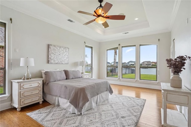 bedroom with a raised ceiling, light wood-style floors, visible vents, and ornamental molding