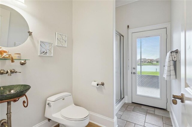 full bath with toilet, baseboards, a stall shower, and stone tile flooring