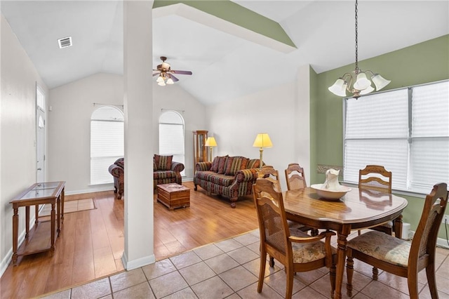 dining space with ceiling fan with notable chandelier, light tile patterned flooring, and vaulted ceiling