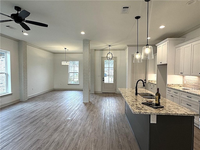 kitchen featuring ceiling fan, sink, decorative light fixtures, white cabinets, and an island with sink