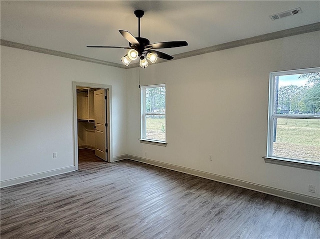 unfurnished bedroom featuring a spacious closet, crown molding, ceiling fan, and dark hardwood / wood-style floors