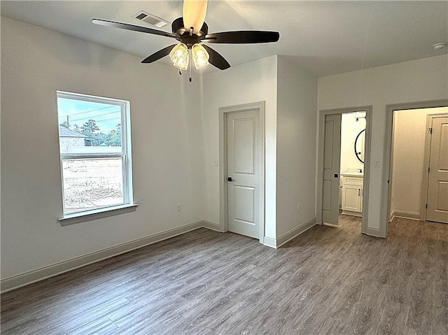 unfurnished bedroom with wood-type flooring, a closet, ensuite bath, and ceiling fan