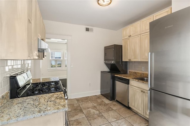 kitchen featuring stacked washing maching and dryer, backsplash, exhaust hood, stainless steel appliances, and light stone countertops