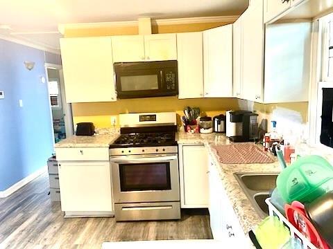 kitchen featuring hardwood / wood-style floors, white cabinets, light stone countertops, ornamental molding, and stainless steel range with gas stovetop