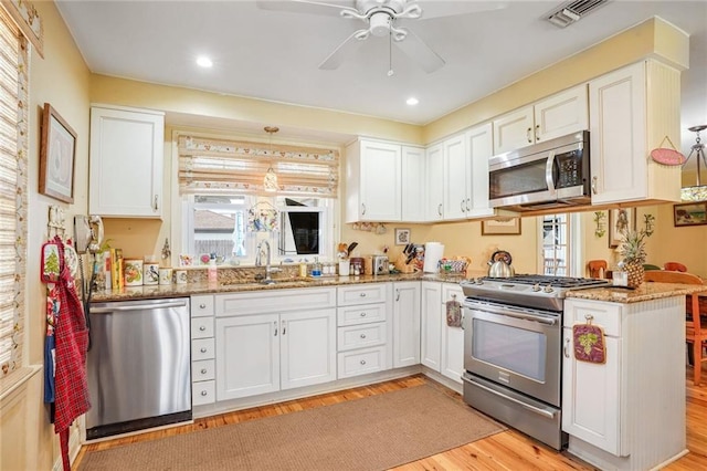 kitchen with sink, kitchen peninsula, appliances with stainless steel finishes, decorative light fixtures, and white cabinetry