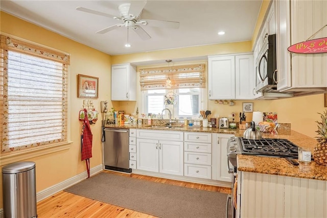 kitchen featuring sink, appliances with stainless steel finishes, stone countertops, white cabinets, and light wood-type flooring