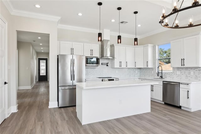 kitchen featuring pendant lighting, a center island, white cabinets, wall chimney exhaust hood, and stainless steel appliances