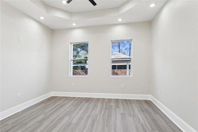 spare room with ceiling fan, a tray ceiling, and light hardwood / wood-style flooring