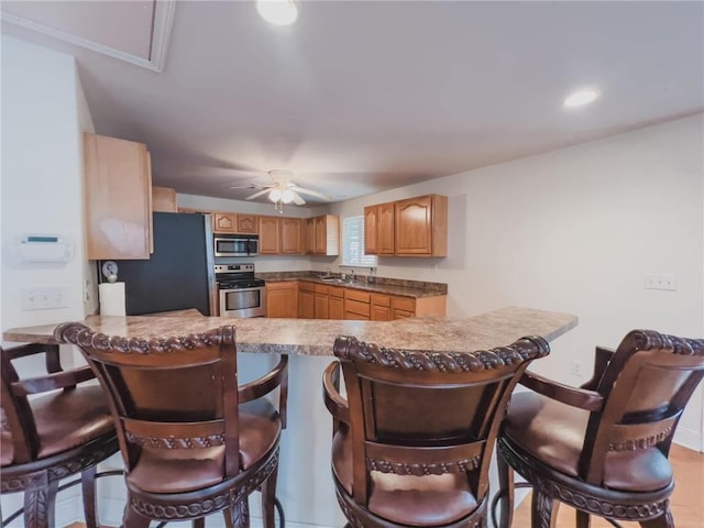 kitchen featuring a breakfast bar, stainless steel appliances, a sink, ceiling fan, and a peninsula