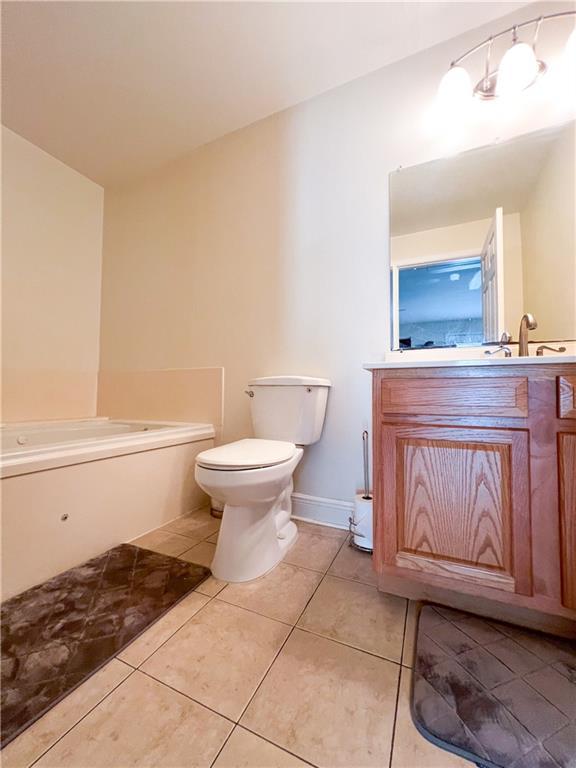 bathroom with tile patterned floors, a tub to relax in, vanity, and toilet