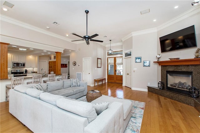 living room featuring french doors, ceiling fan, crown molding, a fireplace, and light hardwood / wood-style floors