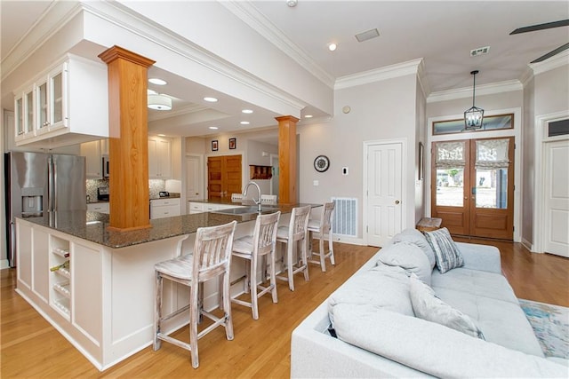 kitchen with a kitchen bar, stainless steel refrigerator with ice dispenser, ornate columns, pendant lighting, and white cabinets