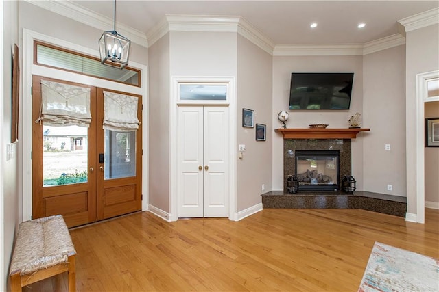 entrance foyer featuring french doors, a high end fireplace, a chandelier, light wood-type flooring, and ornamental molding