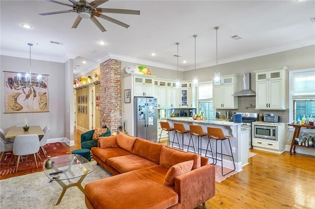 living room with ceiling fan with notable chandelier, light wood-type flooring, and ornamental molding