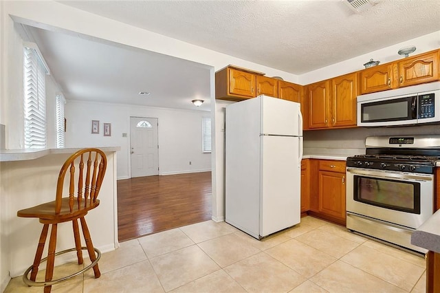 kitchen with light tile patterned floors, gas stove, white fridge, and a textured ceiling