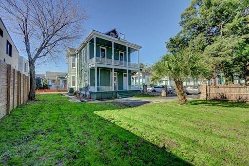 back of property featuring a balcony, covered porch, and a lawn