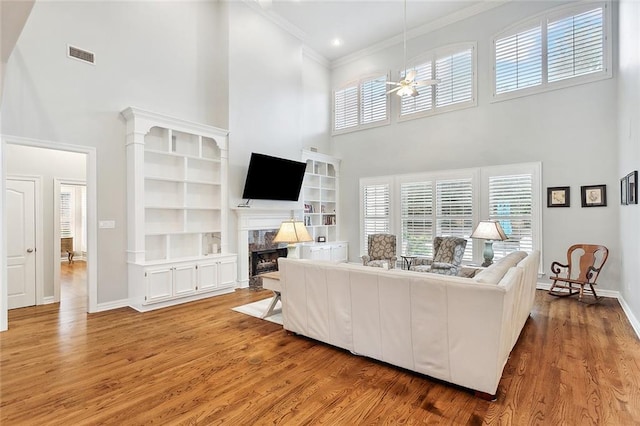 living room with ornamental molding, built in shelves, ceiling fan, a high ceiling, and light hardwood / wood-style floors